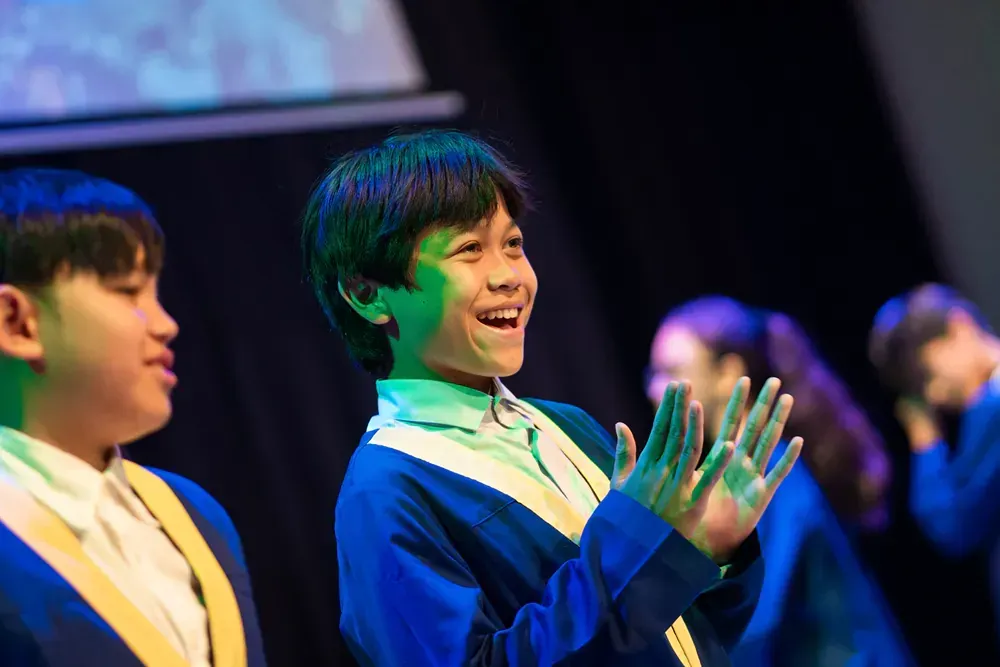 A group of children are standing on a stage clapping their hands.