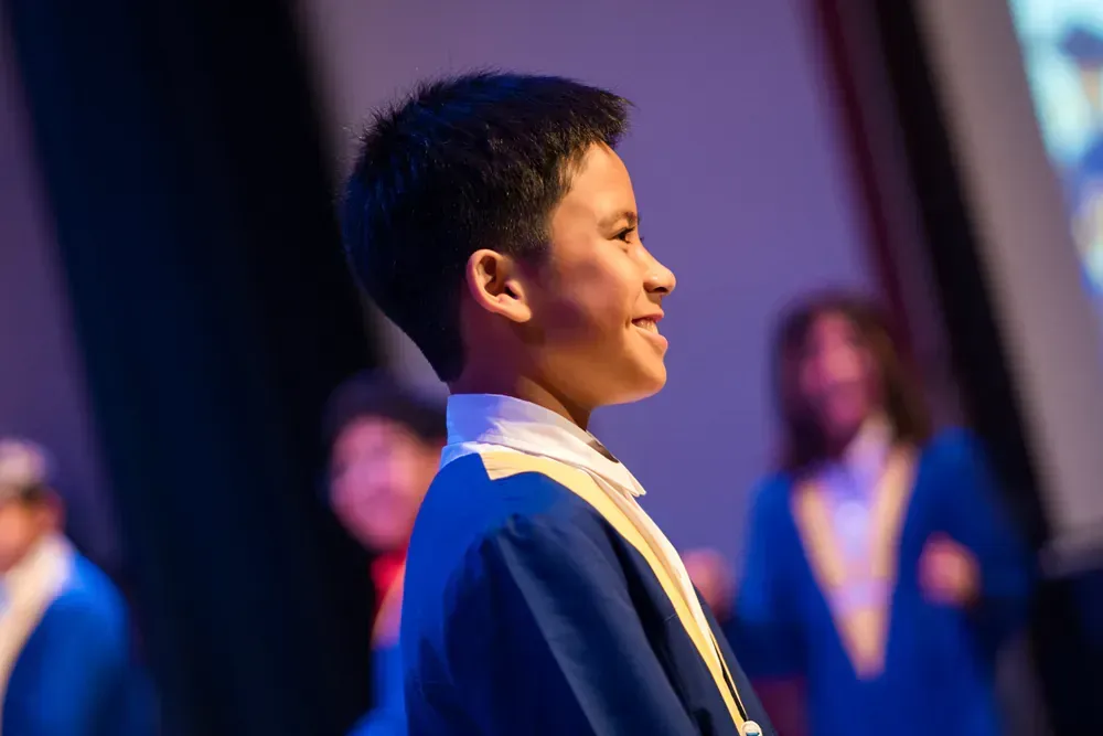 A young boy in a graduation cap and gown is standing on a stage.