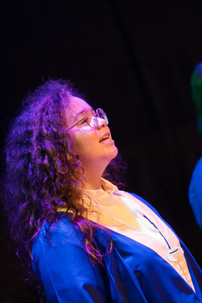 A woman wearing glasses and a blue gown is looking up at the sky.