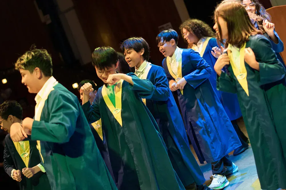 A group of children in graduation gowns are dancing on a stage.