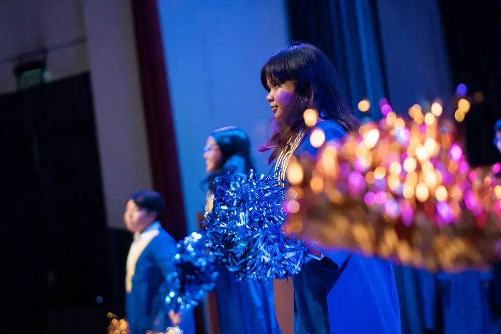 A group of cheerleaders are standing on a stage holding pom poms.