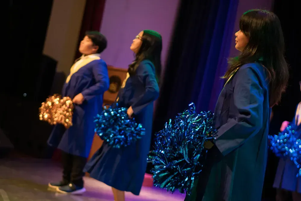 A group of cheerleaders are standing on a stage holding pom poms.