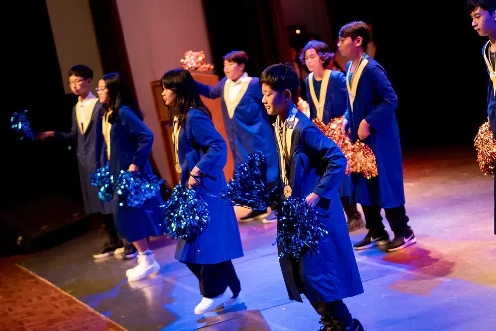 A group of children are dancing on a stage with pom poms.