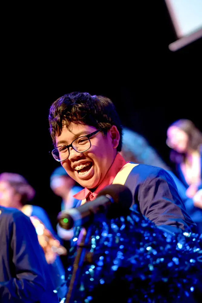 A young man wearing glasses is singing into a microphone on a stage.