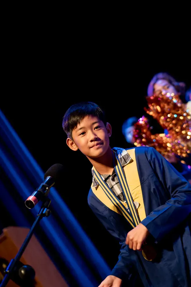 A young boy is standing in front of a microphone on a stage.