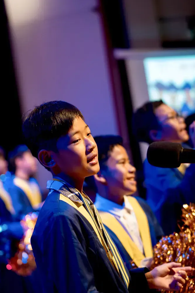 A young boy is singing into a microphone in a choir.