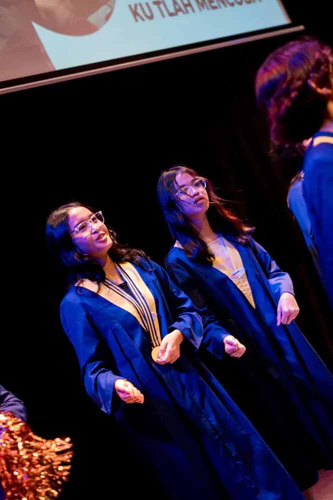 A group of women in blue gowns are dancing on a stage.