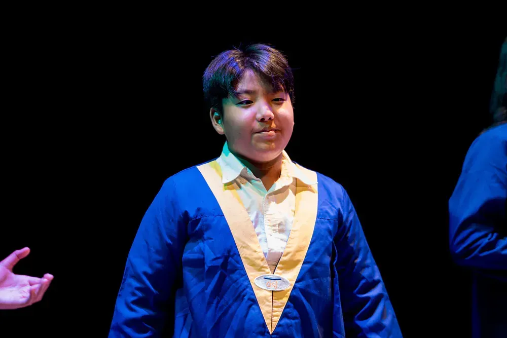 A young boy in a blue and yellow graduation gown is standing on a stage.