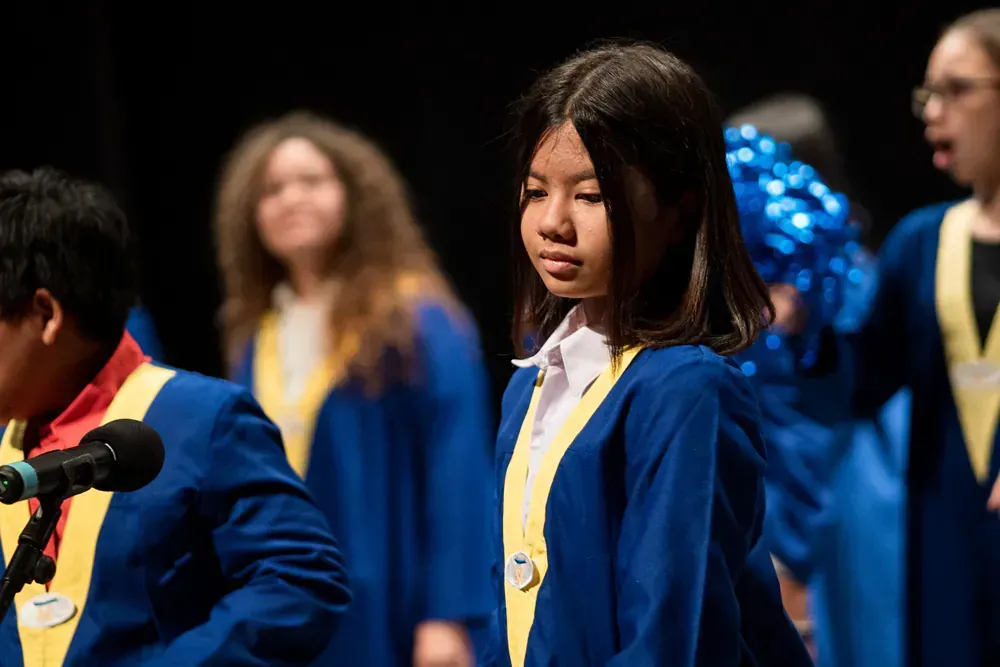 A girl in a blue gown is standing in front of a microphone.