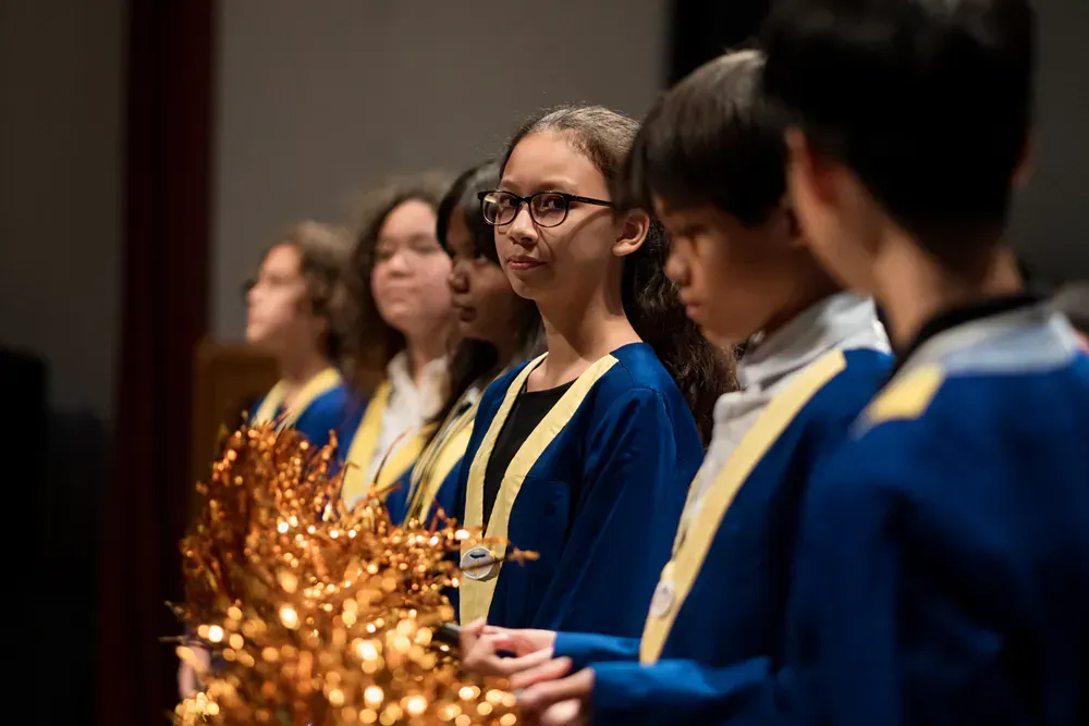 A group of children are standing in a row holding pom poms.