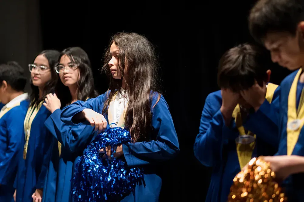 A group of children in graduation gowns are standing on a stage.