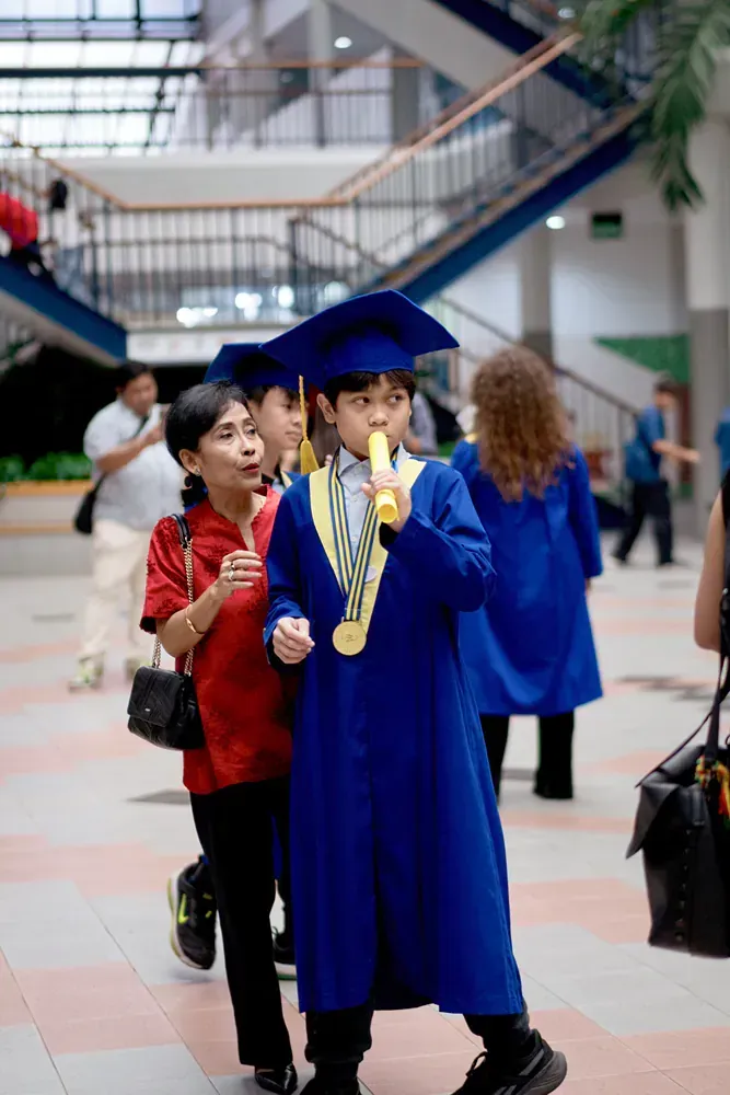 A young boy in a graduation cap and gown is eating a banana.