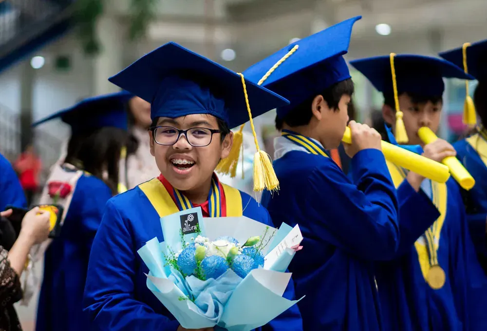 A boy in a graduation cap and gown is holding a bouquet of flowers.