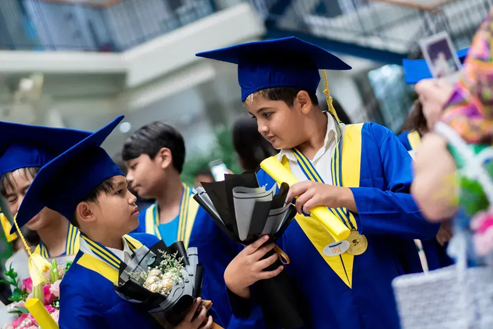 A group of young boys in graduation caps and gowns are holding a bouquet of flowers.