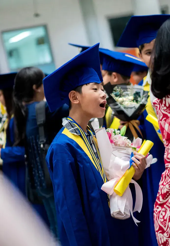 A boy in a graduation cap and gown is holding a bouquet of flowers