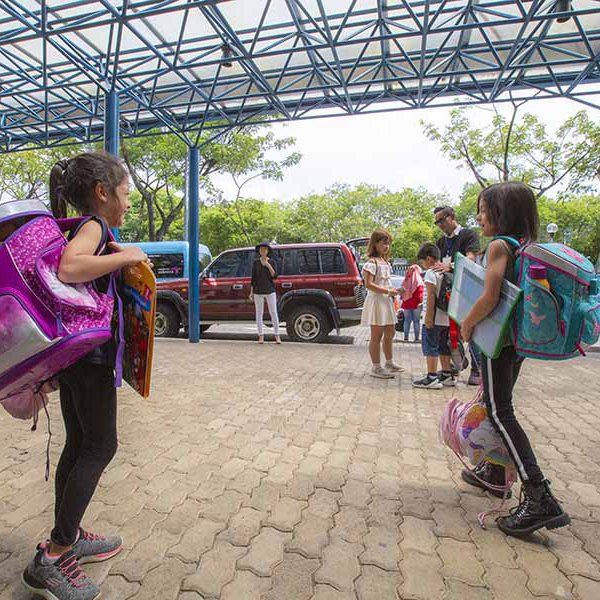 A group of children with backpacks are standing in a parking lot.