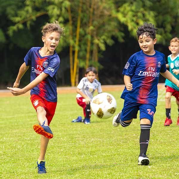 A group of young boys are playing soccer and one of their shirts says fly emirates