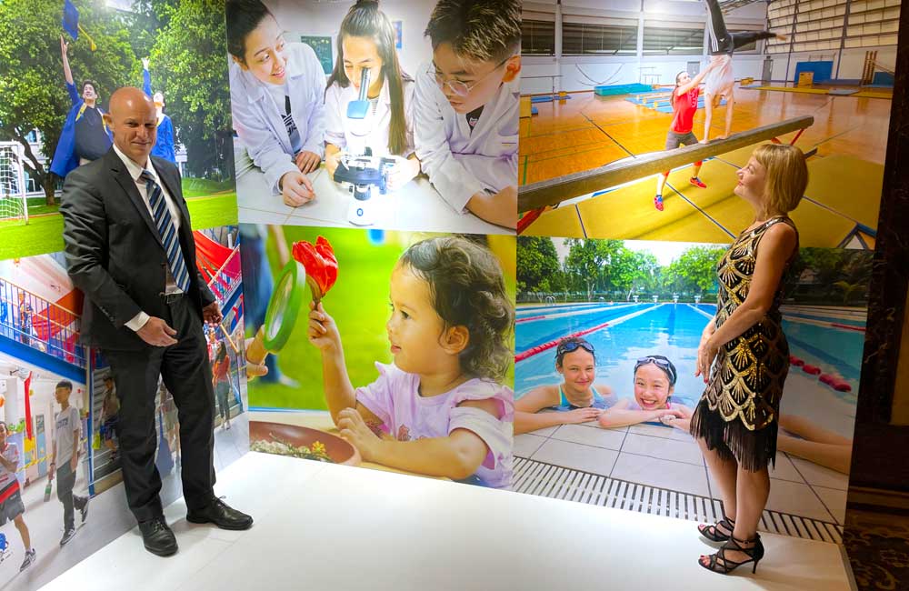A man and a woman are standing in front of a wall with pictures of children.
