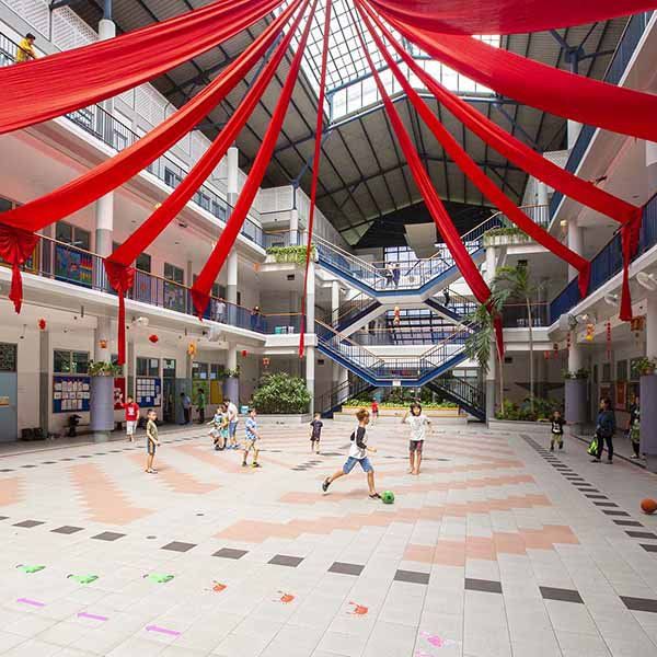A group of children are playing in a large building with red flags hanging from the ceiling.
