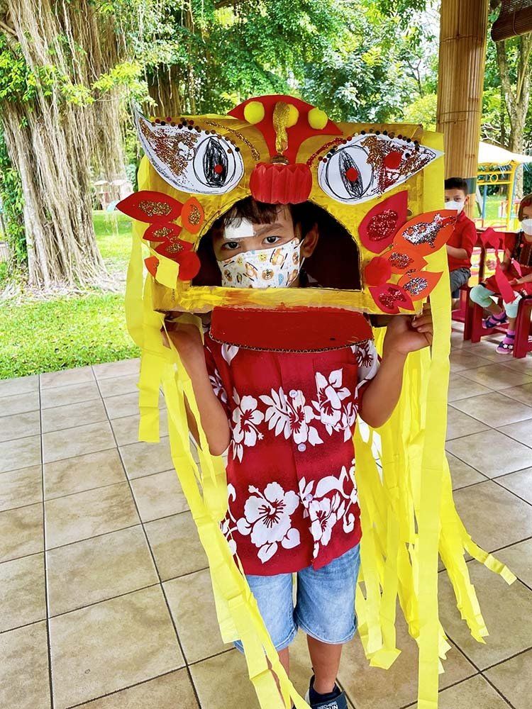 A child is wearing a mask and holding a cardboard lion head.