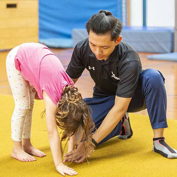 A man is helping a little girl do a handstand on the floor.