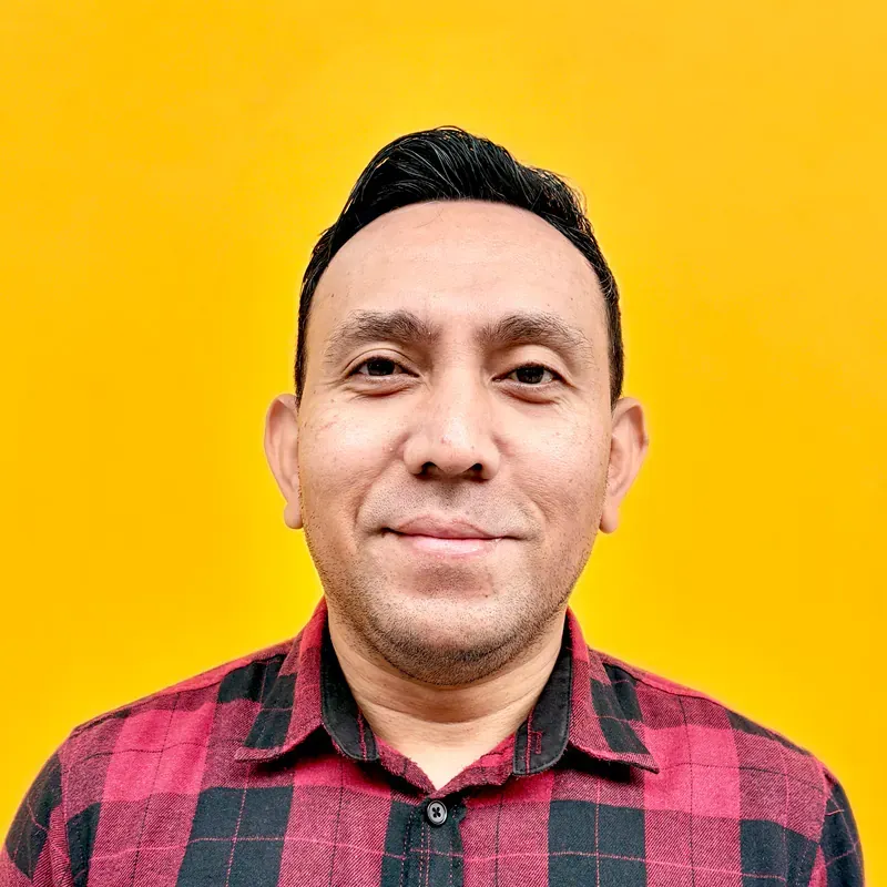 A man with a beard is wearing a plaid shirt and taking a selfie.