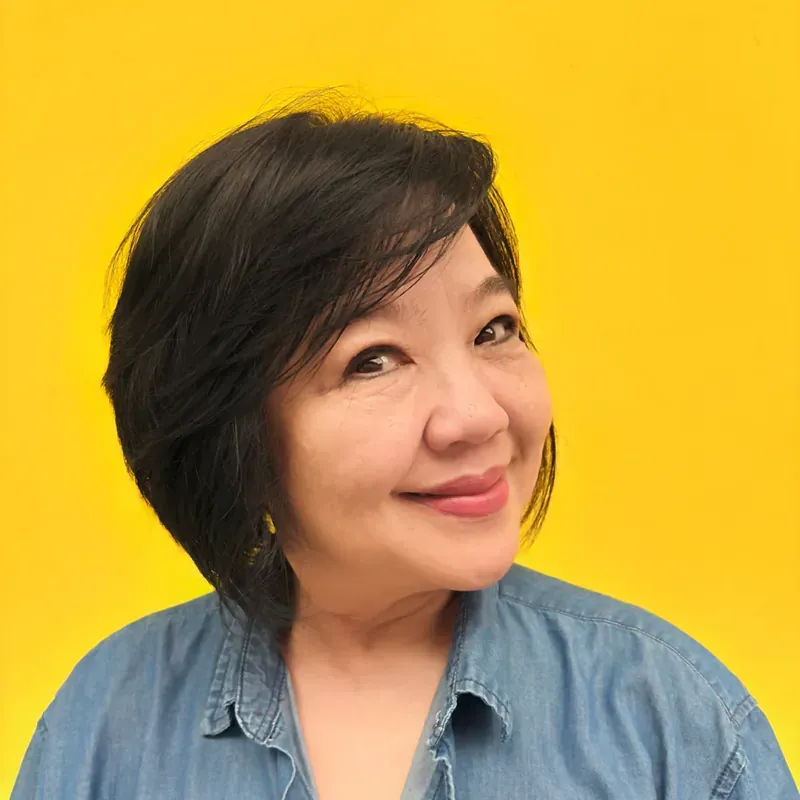 A woman with short black hair is smiling and wearing a floral shirt.