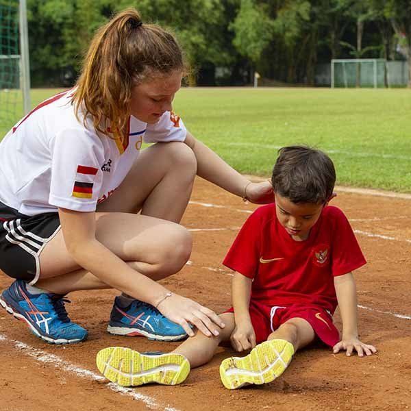 A woman is kneeling down next to a young boy who is sitting on the ground