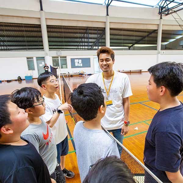 A man is talking to a group of young boys in a gym