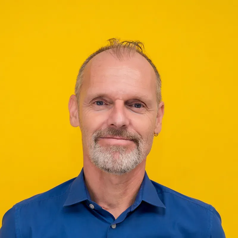 A man with a bald head is wearing a pink shirt and smiling.