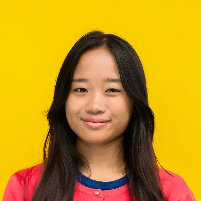 A young woman with long black hair is standing in front of a staircase.