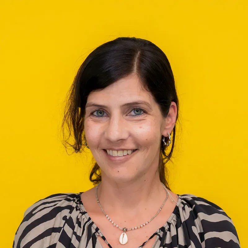 A woman in a black shirt and necklace is smiling while sitting at a table.