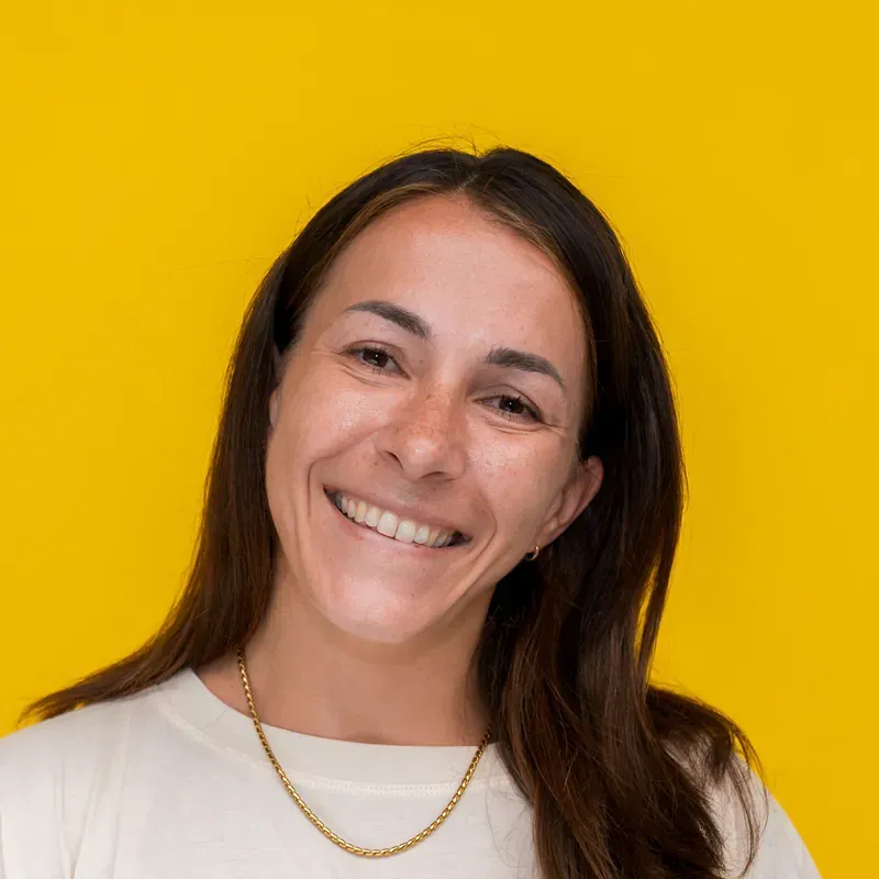 A woman in a black shirt and necklace is smiling while sitting at a table.