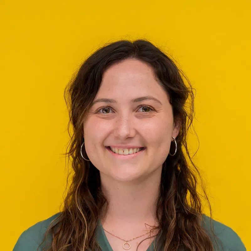 A woman in a black shirt and necklace is smiling while sitting at a table.