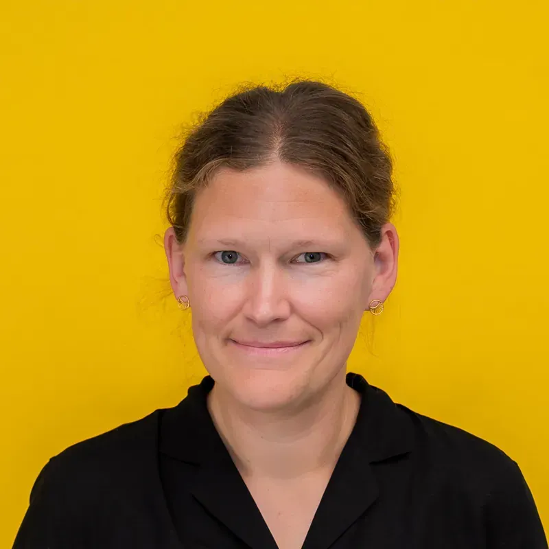 A woman in a striped shirt is standing in front of a white wall.