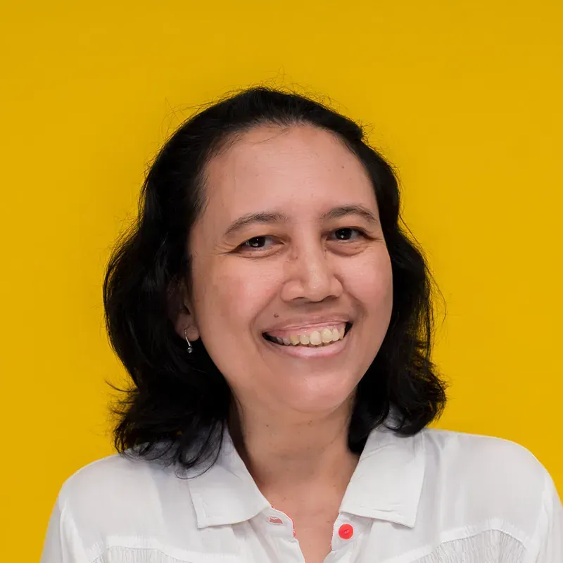 A woman in a yellow shirt is smiling in front of a blue curtain.