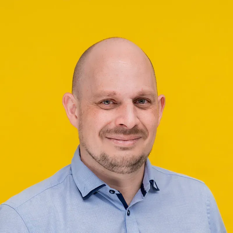 A bald man with a beard is smiling for the camera while wearing a blue shirt.