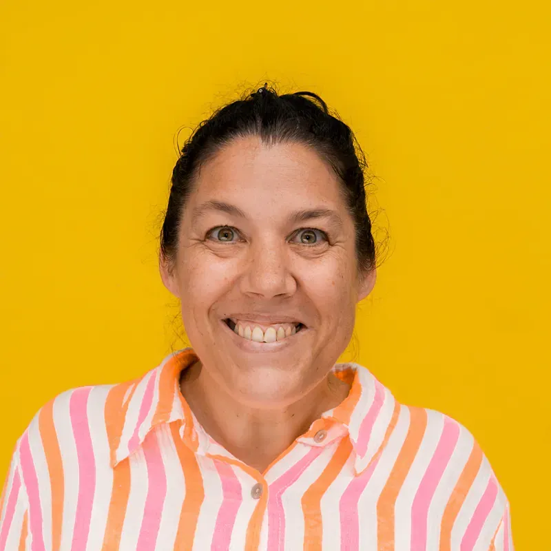 A woman in a brown shirt is smiling in front of a building.