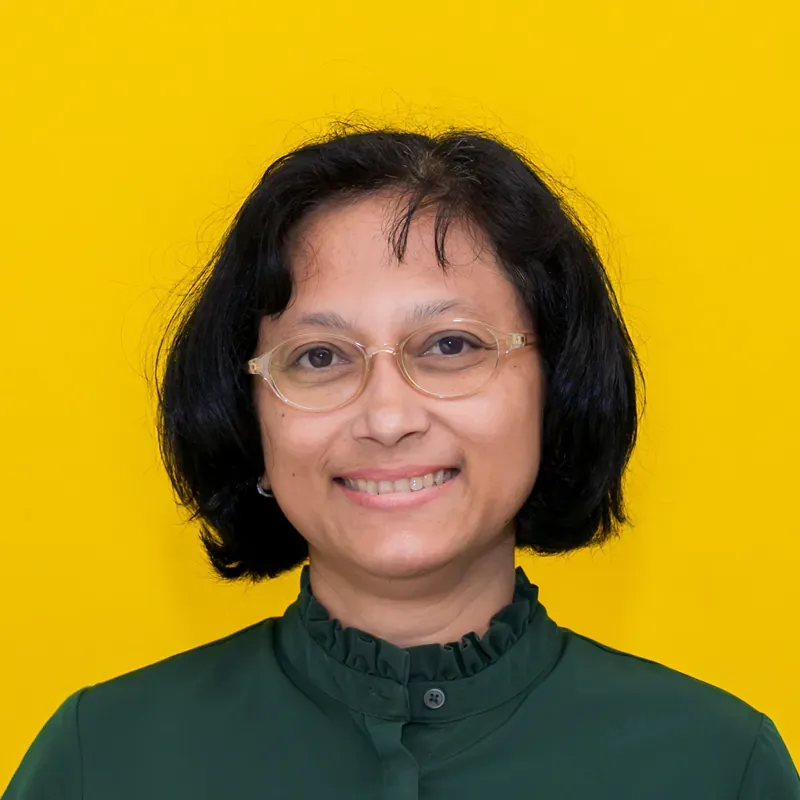 A woman wearing glasses and a pink shirt is smiling for the camera.