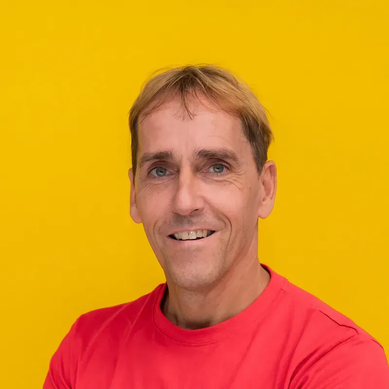A man wearing sunglasses and a pink shirt is holding a red traffic cone