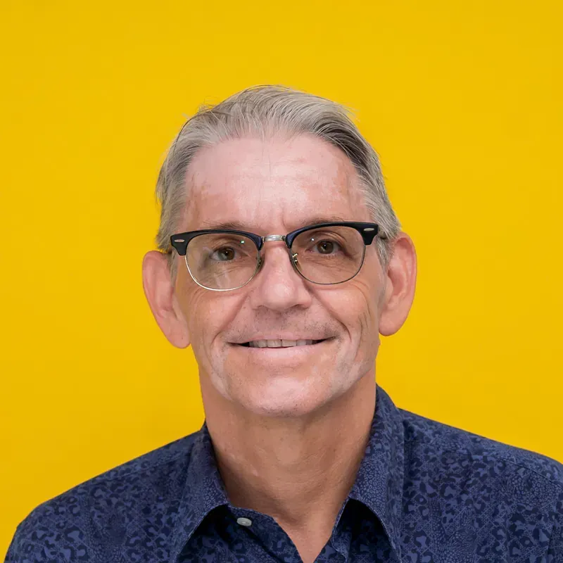 A man wearing glasses and a red shirt is smiling for the camera.
