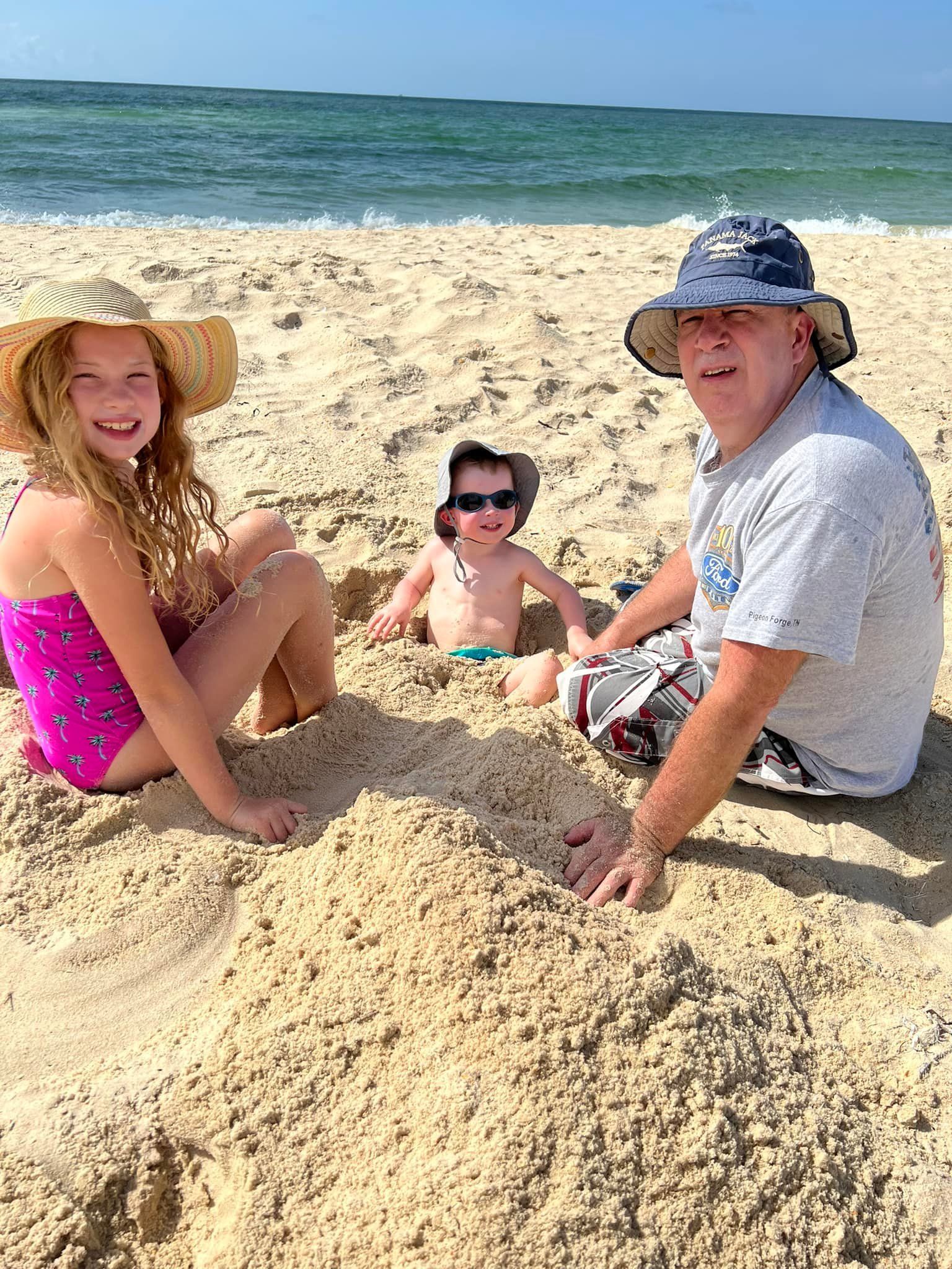 a man and two children are playing in the sand on the beach .