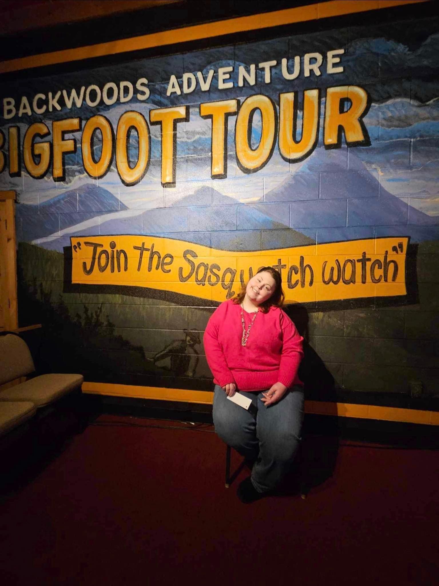 a woman sitting in front of a bigfoot tour sign