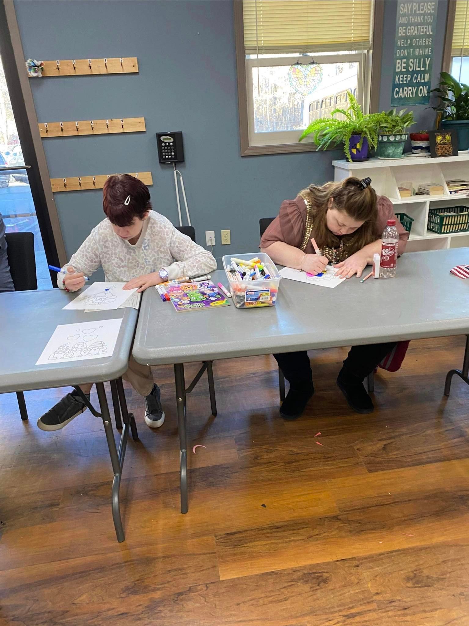 two people are sitting at a table drawing on a piece of paper .