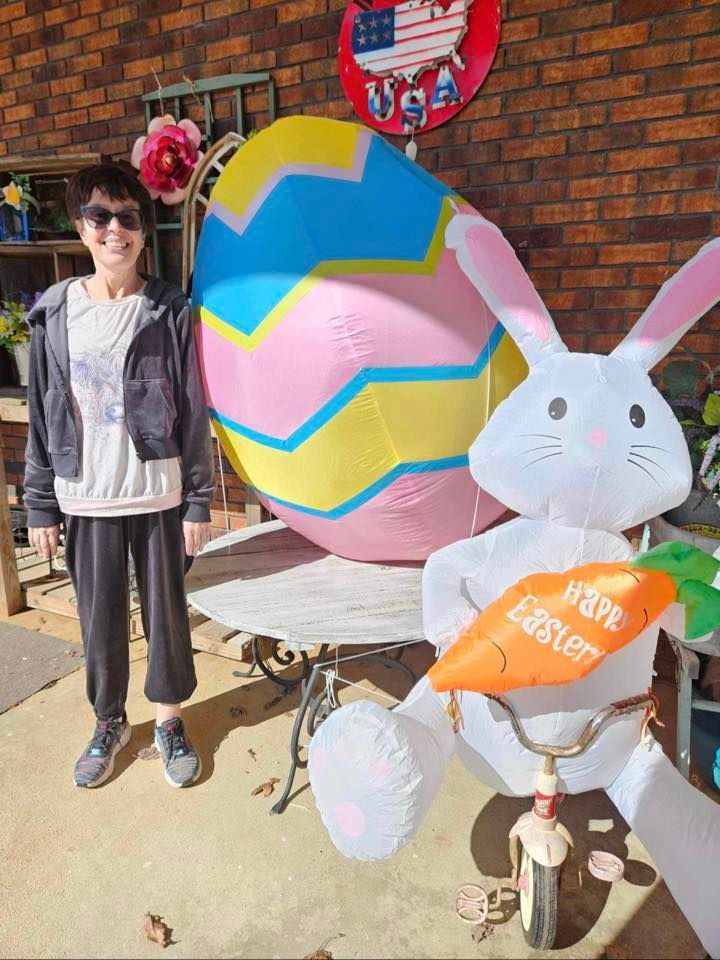 a woman is standing next to a giant easter egg and a bunny on a bike .