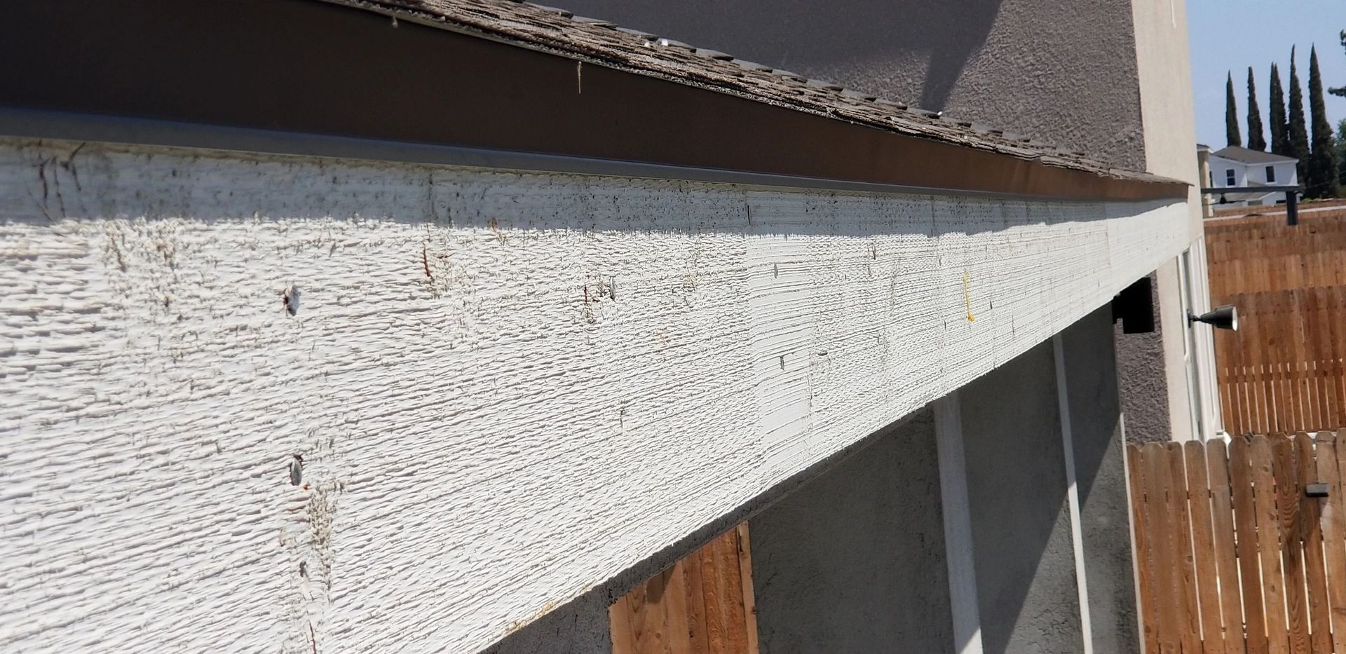 A close up of a concrete wall with a wooden fence in the background.
