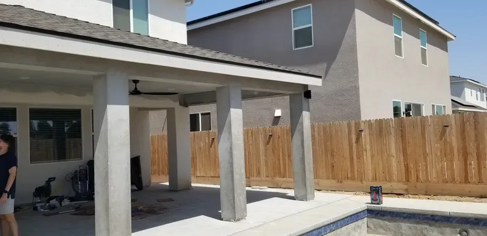 A woman is standing under a covered patio next to a pool.