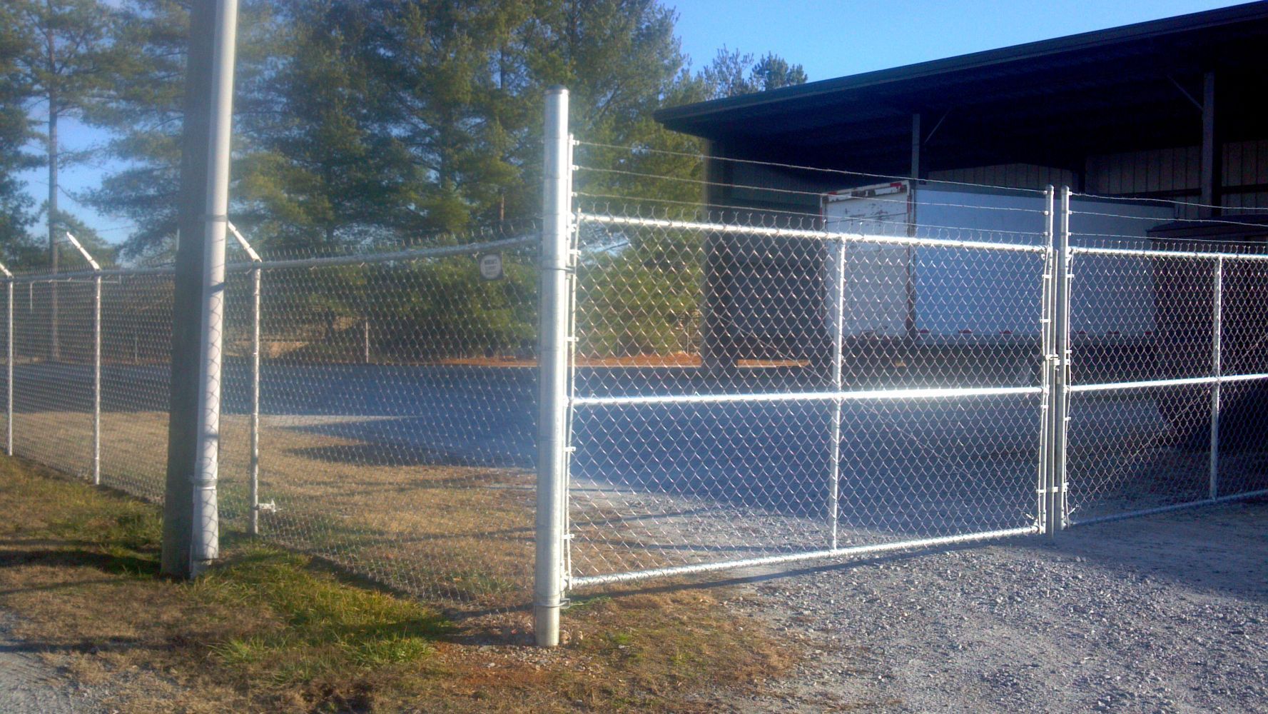 Chain link fence with a gate, in front of a building and trees.