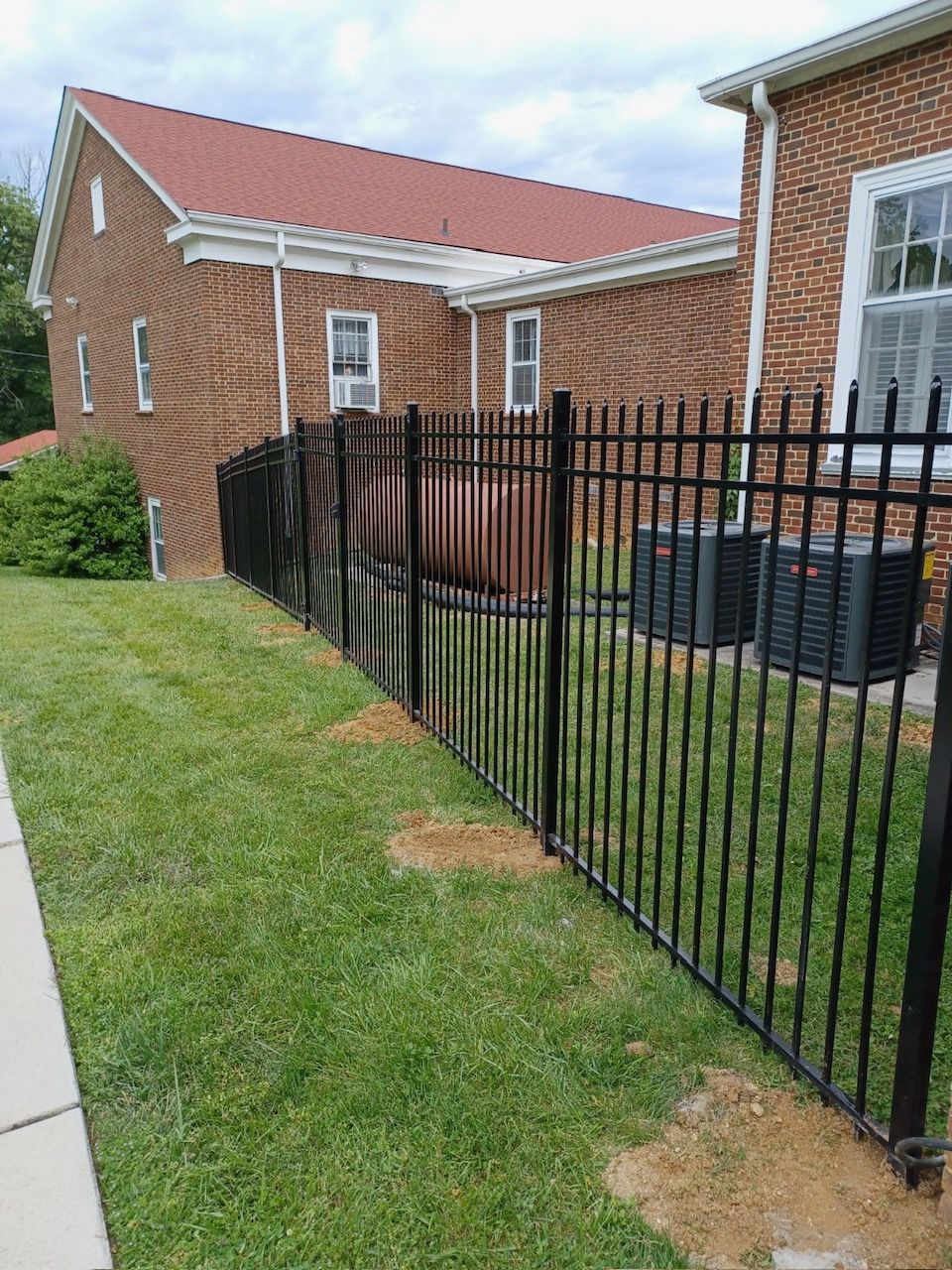 Black metal fence along a grassy lawn next to a brick building.