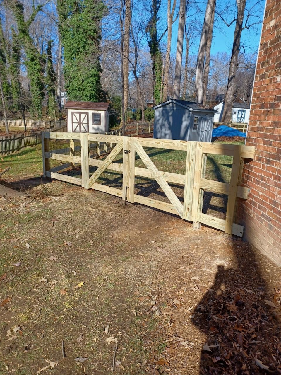 Wooden gate built into a brick wall, with a grass yard in front. Other sheds and trees in the background.